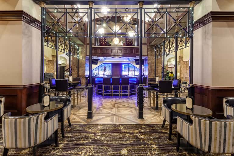 Elegant hotel lounge with metallic railings, purple lighting, and round seating areas