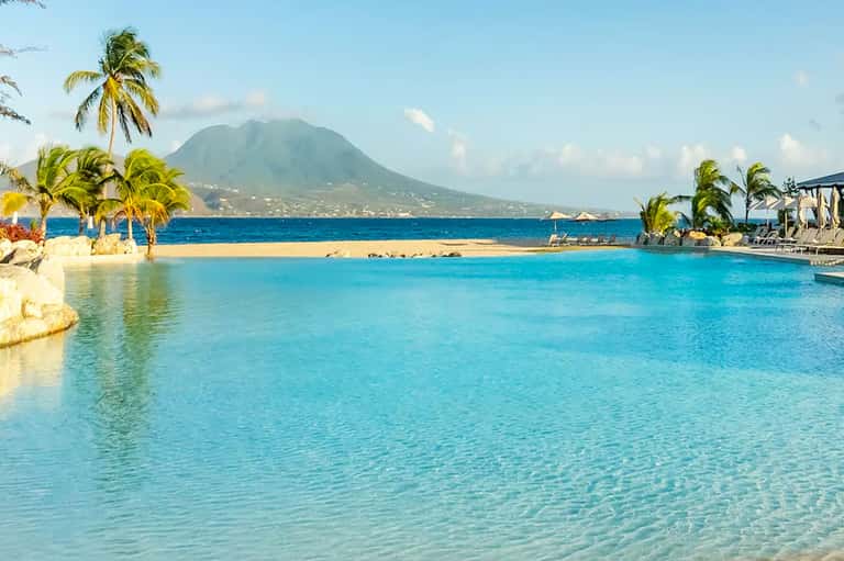Turquoise lagoon pool with palm trees and volcanic mountain backdrop at tropical beach resort