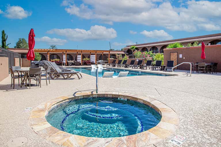Resort pool area with circular hot tub, main pool, umbrellas, and brick buildings