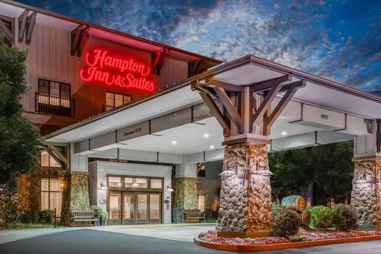 Hampton Inn & Suites entrance at dusk with neon sign and wooden architectural details