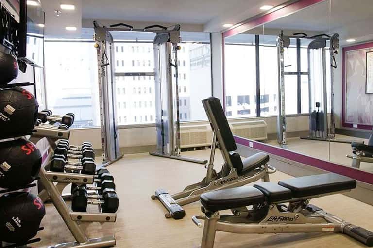 High-rise fitness center with dumbbells, weight machines, mirrors, and city views through windows