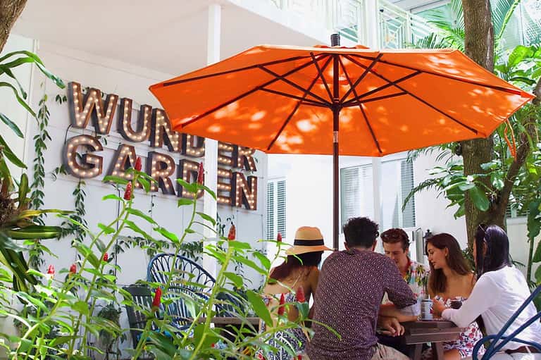 Outdoor garden dining area under orange umbrella with group of guests and lush tropical plants