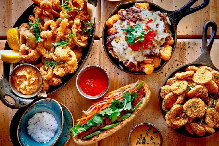 Cast iron skillet appetizers including shrimp, croquettes, pizza and dipping sauces on wooden table