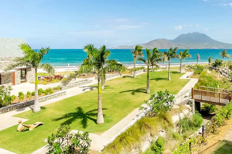 Beachfront resort grounds with palm trees, manicured lawn, and ocean view with volcanic mountain