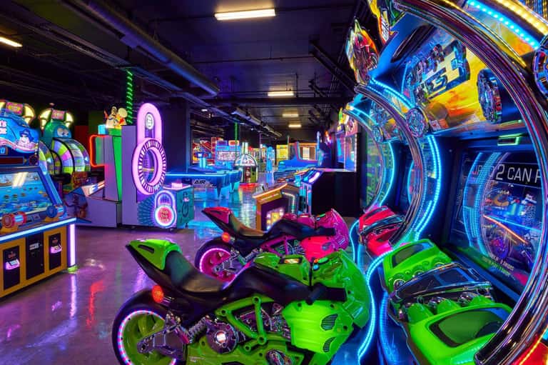 Vibrant arcade game room with neon-lit racing bikes, vintage games, and colorful lighting