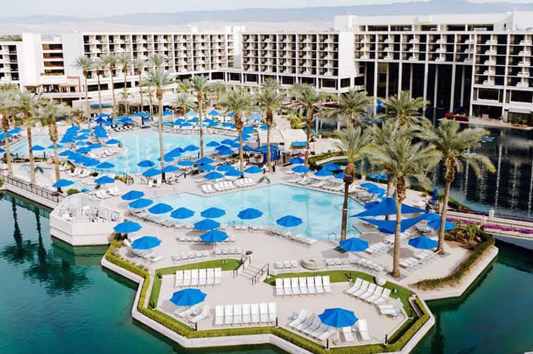 Resort pool area with blue umbrellas, palm trees, and modern white buildings
