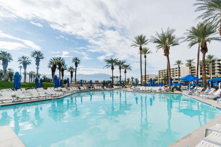 Large rectangular pool with blue umbrellas, palm trees, and mountain views