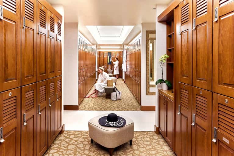Spa locker room with wooden lockers lining both sides and attendant in white spa attire