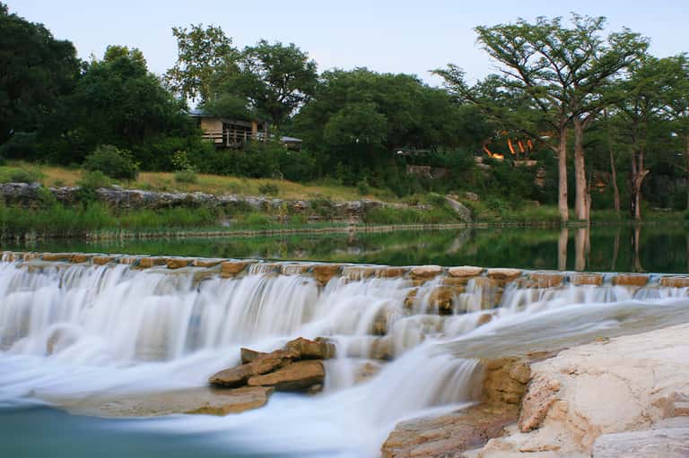 Waterfall flowing into turquoise pool with lodge buildings and trees in background