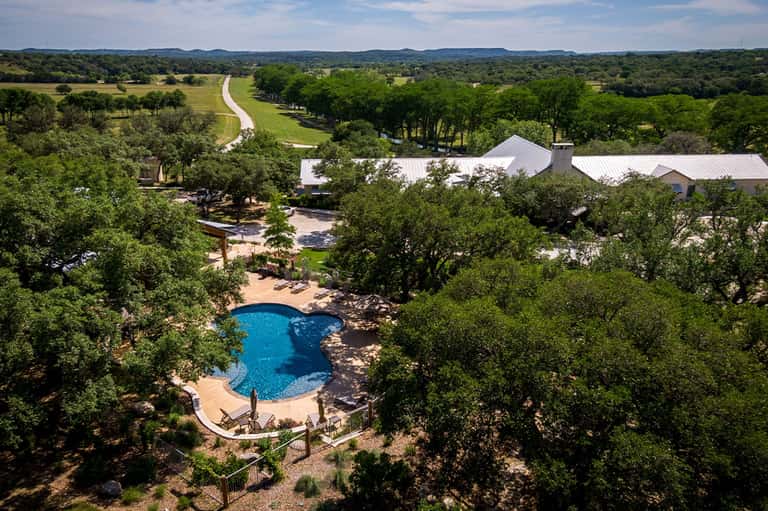 Aerial view of luxury resort pool nestled in trees with white buildings and river