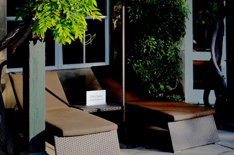 Outdoor seating area with woven chairs under pergola surrounded by lush green foliage