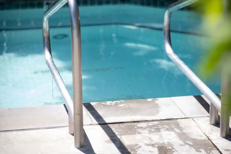 Swimming pool access with chrome handrails and concrete deck stairs