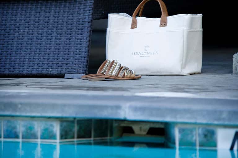 White spa tote bag and striped sandals displayed poolside at luxury resort wellness center