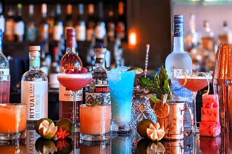 Colorful cocktails at resort bar with spirits bottles, tropical garnishes, and ambient lighting