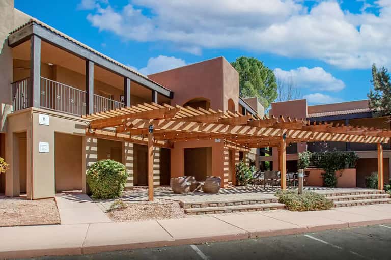 Modern terracotta-colored resort building with wooden pergola, terrace, and desert landscaping