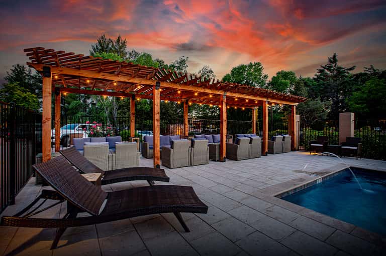 Resort pool deck at dusk with wooden pergola, seating area, lounge chairs, and glowing lights
