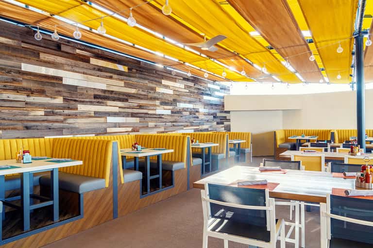Modern rooftop restaurant with yellow fabric ceiling, wood accent wall, and bright seating areas