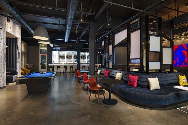 Modern recreational space with pool table, curved black sectional sofa, pendant lighting, and industrial ceiling
