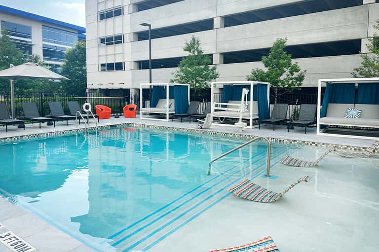 Modern hotel pool with blue loungers, cabanas, and red accent chairs