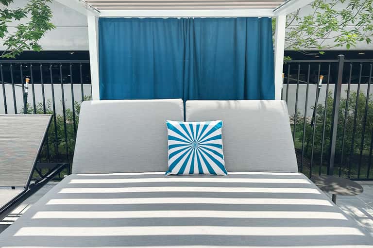 Modern cabana bed with white cushions and blue curtain backdrop on rooftop terrace