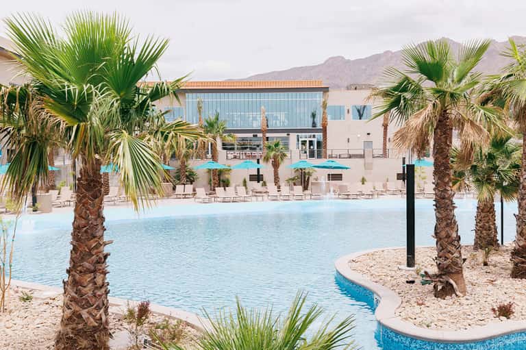 Resort lagoon pool surrounded by palm trees with turquoise umbrellas and modern building