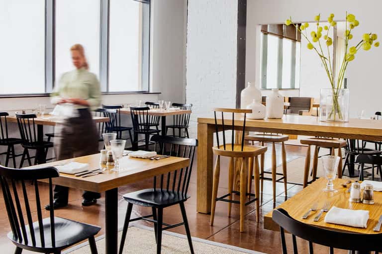 Contemporary hotel restaurant interior with wooden tables, black chairs, large windows, and white flowers