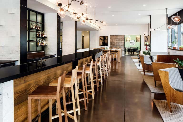 Contemporary restaurant and bar interior with white brick, wooden seating, pendant lighting, and open layout