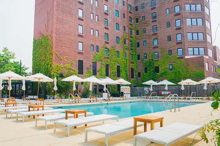 Urban pool deck with lounge chairs, umbrellas, ivy-covered brick building, and bright turquoise water