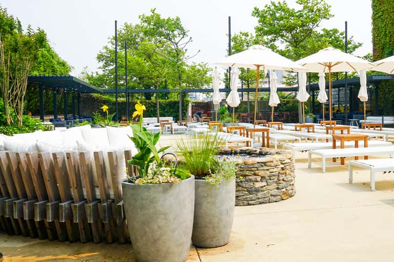 Modern outdoor patio with white umbrellas, wooden tables, planters, and black pergola structure