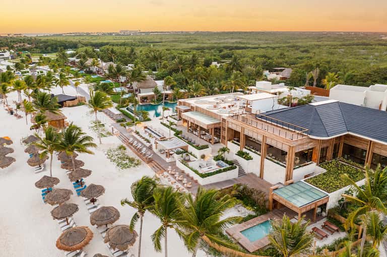 Aerial view of beachfront resort with white sand, palm trees, and wooden structures