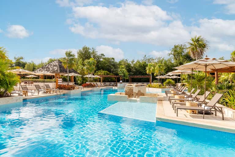 Resort pool with loungers, umbrellas, shallow lounge area, and tropical landscape