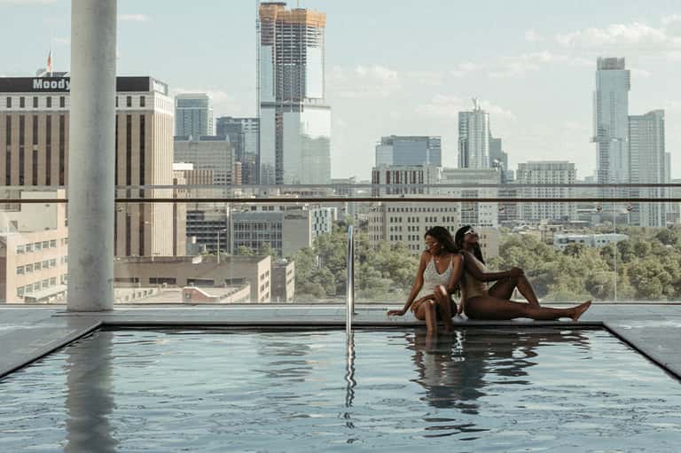 Two women relaxing in rooftop infinity pool with cityscape view of downtown skyline