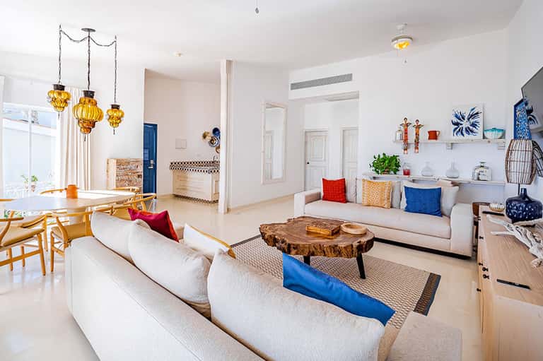 Bright modern living room with cream sofas, wooden furniture, blue accents, and golden hanging light fixtures