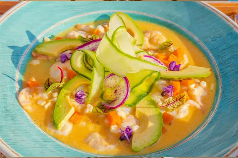 Culinary plating of shrimp dish with avocado, edible flowers on turquoise plate