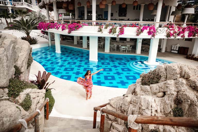 Resort pool with vibrant blue tile pattern and bright pink flowers draped above white columns