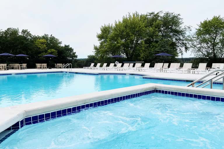 Outdoor pool with spa feature, loungers with umbrellas, and tree-lined landscape
