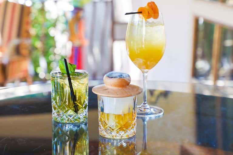 Three colorful tropical cocktails on bar counter with mint garnish and orange slice decorations