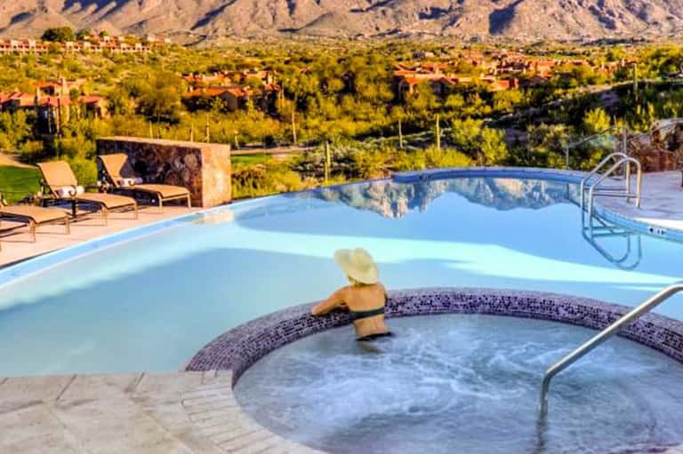 Resort pool with hot tub in foreground, mountain views, desert landscape, and lounge chairs