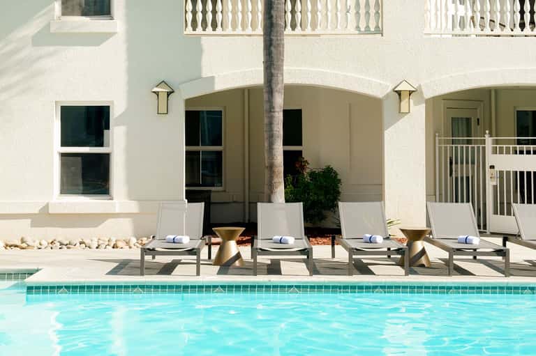 Poolside loungers against white building with arches and palm tree at upscale resort