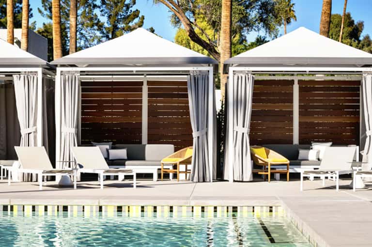 Luxury poolside cabanas with white canopies and lounge seating beside a resort pool and palm trees