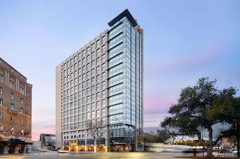 Modern hotel high-rise building with tan and glass facade at dusk with street-level retail