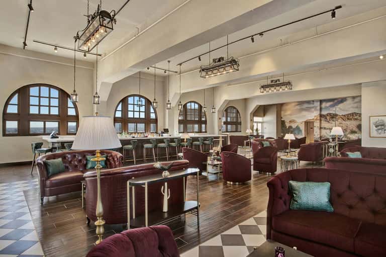 Elegant hotel lounge with burgundy leather seating, arched windows, and classic pendant lighting