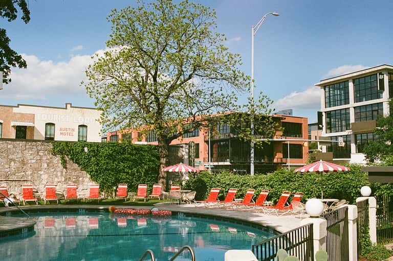 Resort pool with red lounge chairs, hedges, and historic brick buildings