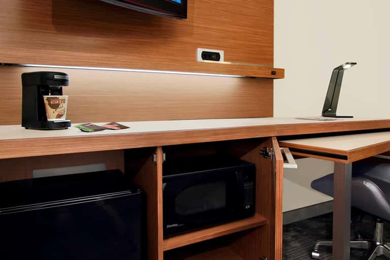 Hotel room desk with wood paneling, coffee maker, TV, and modern office setup