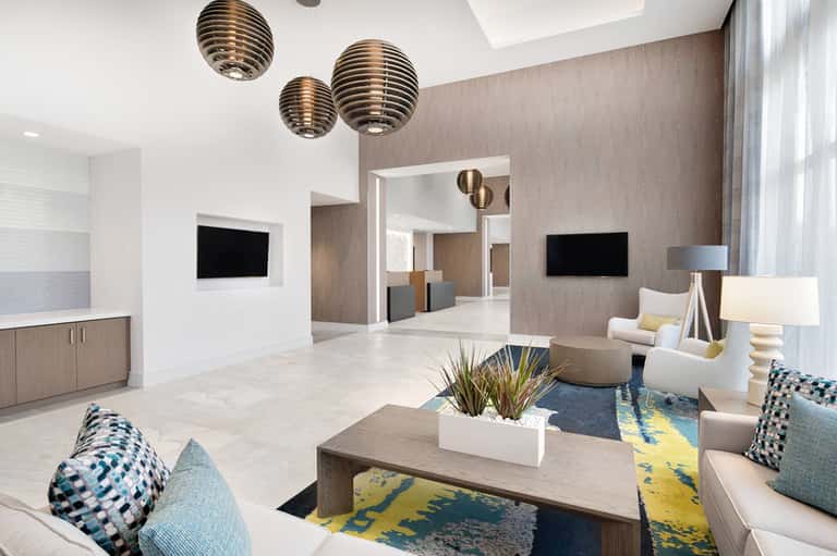 Modern hotel lobby with wooden pendant lights, neutral furnishings, and patterned rug