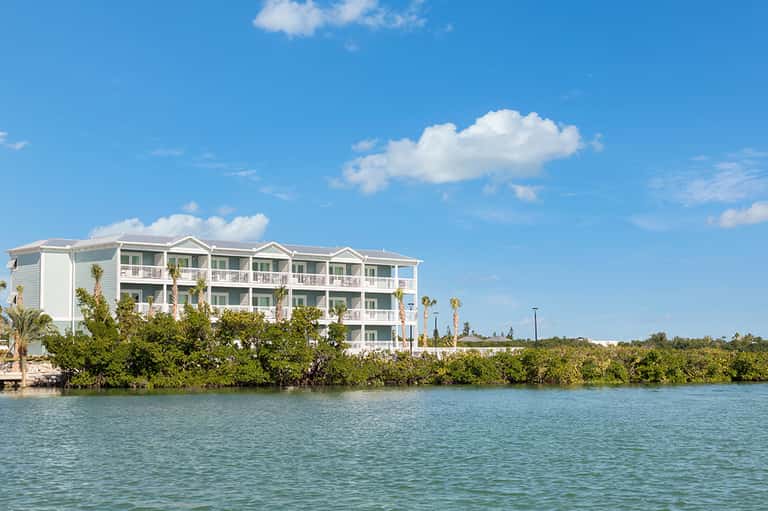 Waterfront hotel with white facade and palm trees along calm turquoise bay
