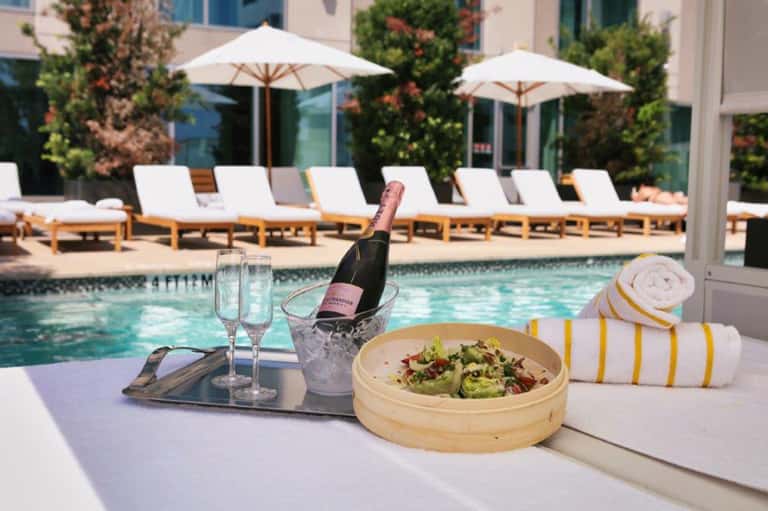 Poolside champagne and salad setup with loungers, umbrellas, and resort facilities in background