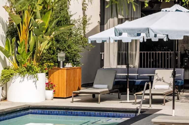 Resort pool deck with lounge chairs, white umbrella, and lush landscaping