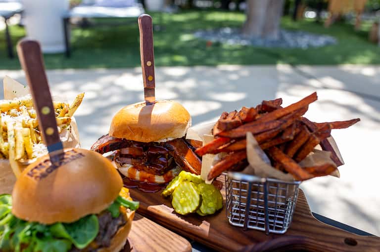 Gourmet burger with sweet potato fries and condiments on wooden board at beachside restaurant