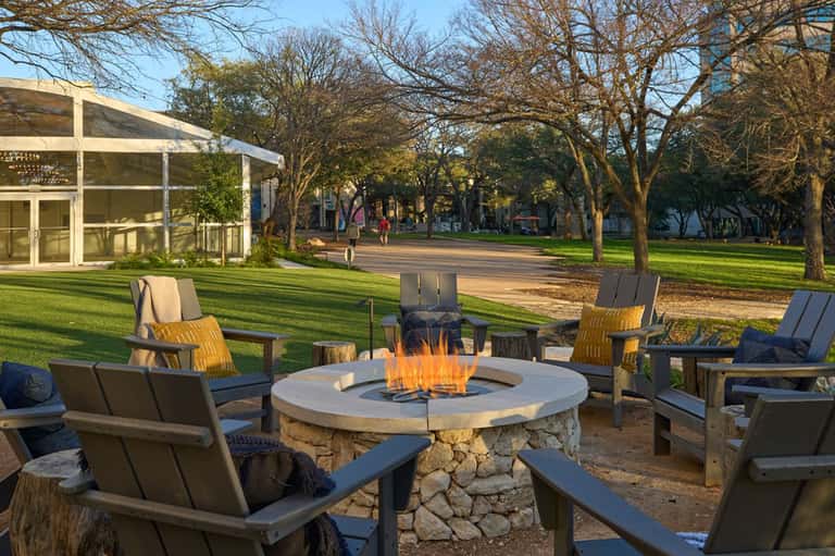 Outdoor fire pit seating area surrounded by trees with green lawn